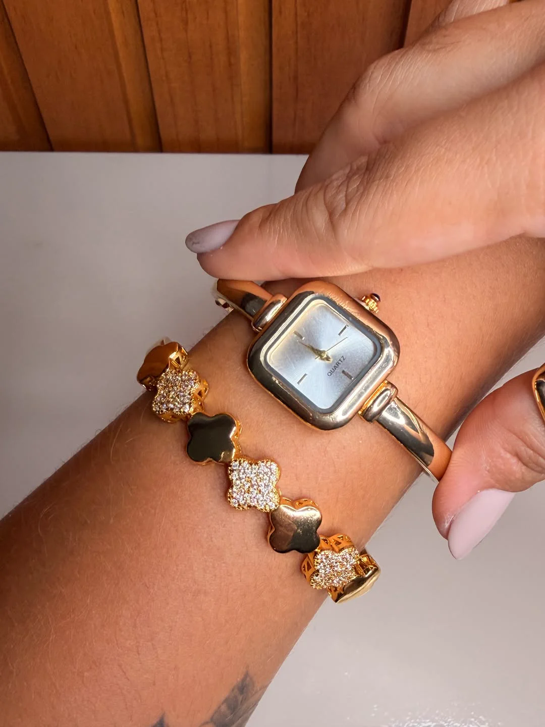 Relógio bracelete feminino dourado acompanhado de pulseira de trevos cravejados com zircônias